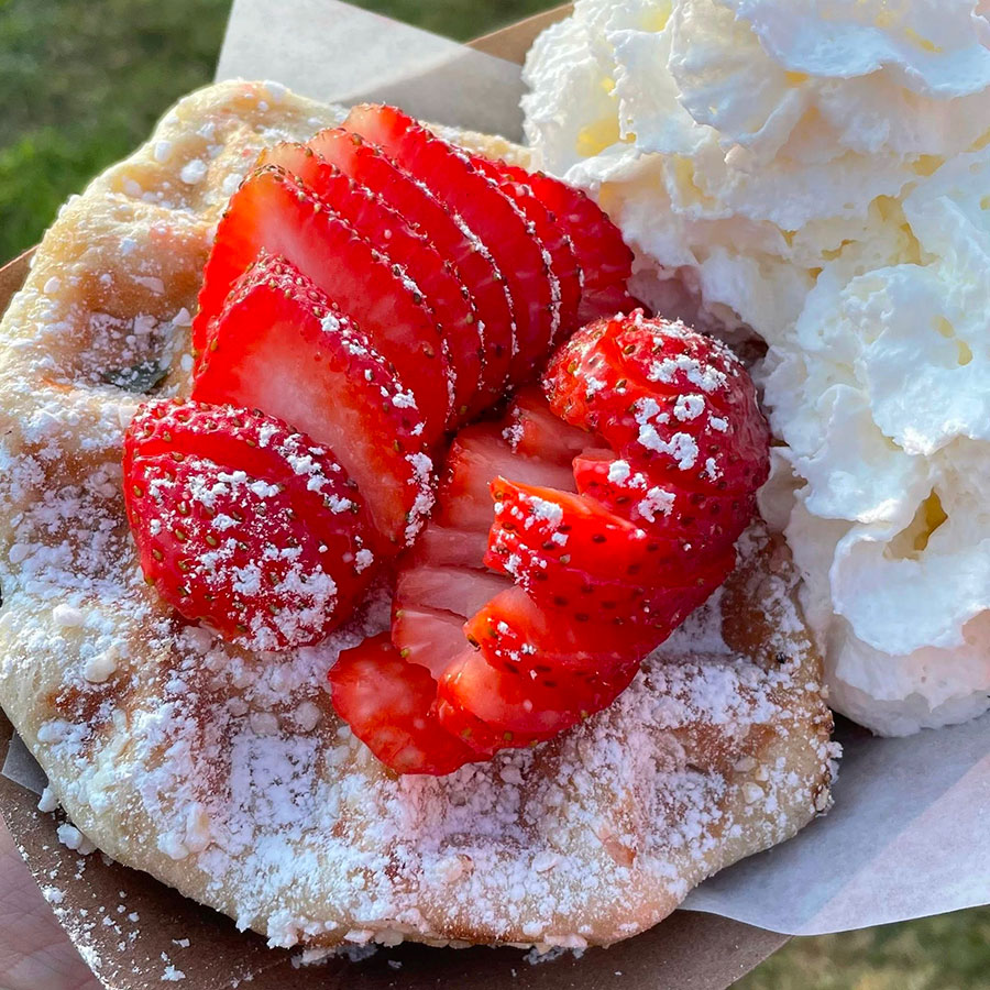 Marty’s waffle with a dusting of powdered sugar with a mound of sliced strawberries on top and a mound of whipped cream on the side